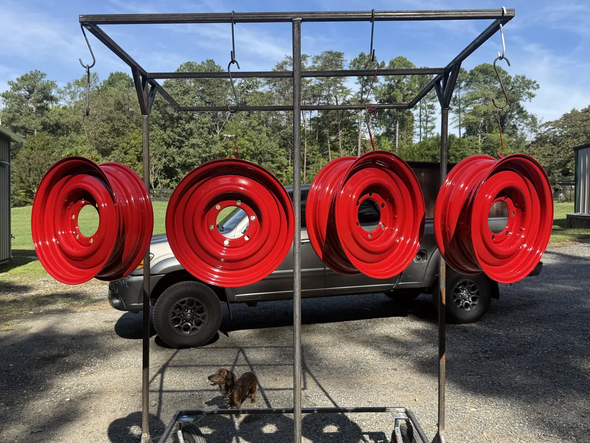 Set of four steel wheels powder coated gloss red, hanging on the cure rack